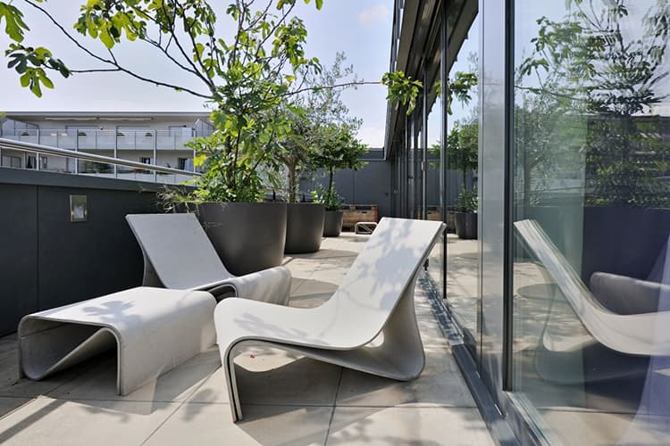 Greenform sculptural outdoor lounge chairs from the Sponek line up against a full wall of windows