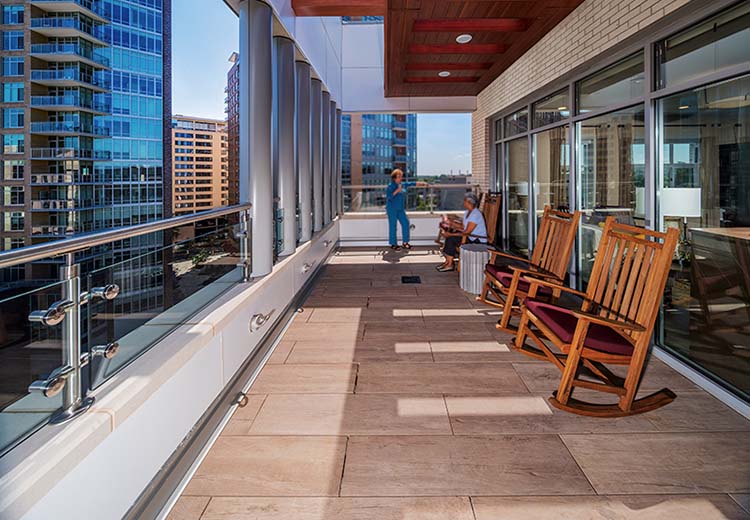 Balcony of a high-rise residence lined with rocking chairs. The flooring is large Hanover porcelain pavers in a terracotta color.