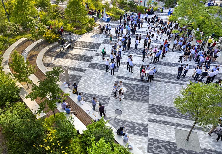 Overhead view of a plaza in front of a multi-story corporate building. People dressed in business attire are gathered in small groups, chatting. Hanover Prest Pavers are on the grounds in the Cummins pattern.
