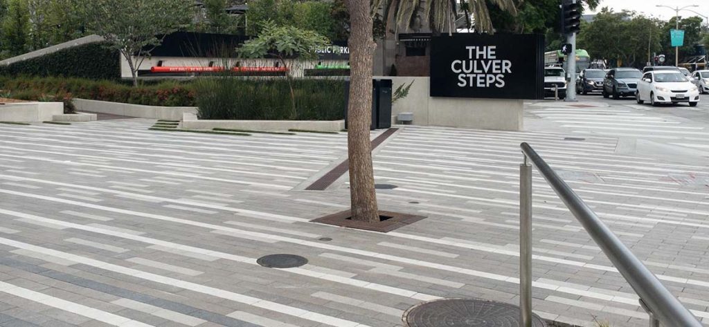 Outdoor plaza with random stripes of color in the Ironsmith Paver grates. A sign saying "The Culver Steps" is in the distance.