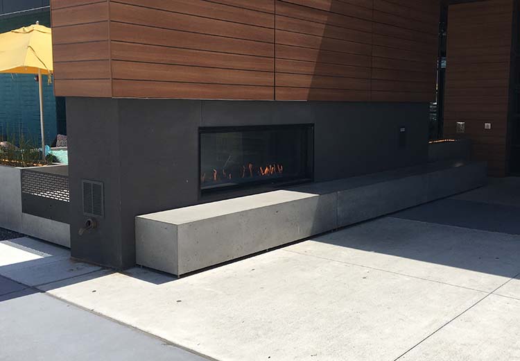 An outdoor restaurant fireplace with a Form and Fiber concrete box bench in front.