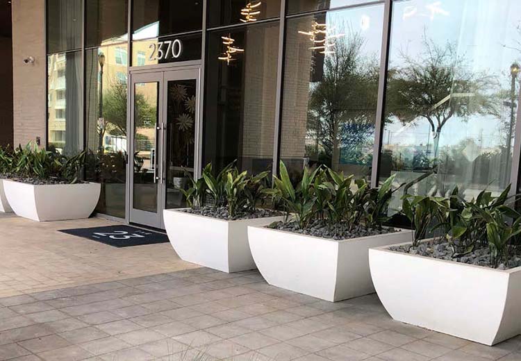 Row of low Form and Fiber Concrete Essentials white planters up against the front glass walls of a large corporate building.