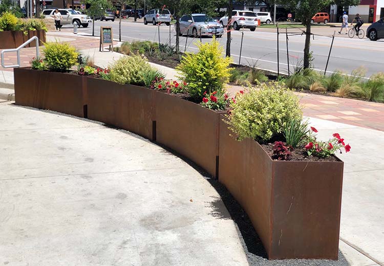 Four Form and Fiber custom Corton steel planters placed end-to-end. They are curved and form a semi-circle.