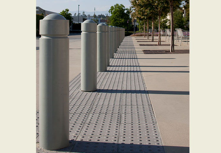 A large walkway is separated from a driveway with a row of Ironsmith Cypress-style modern bollards.