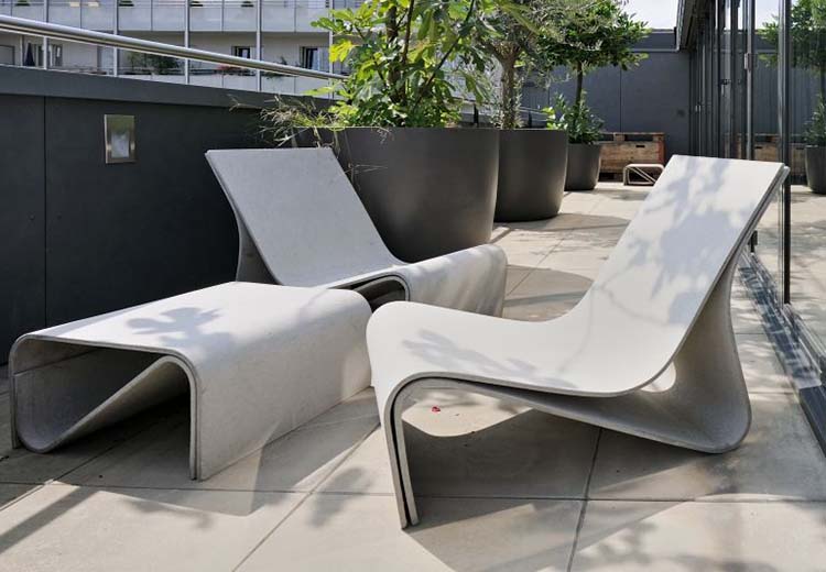 A thin, long apartment balcony with 2 modern-looking cement lounge chairs by Greenform and a matching ottoman from their Sponek line