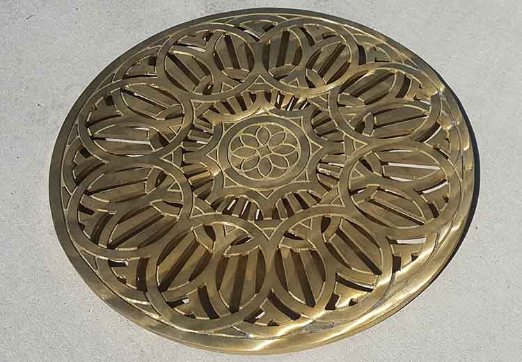 An Ironsmith round drain grate with a decorative circular flower pattern from the Del Sol line is shown in a bronze finish