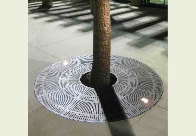 Ironsmith round tree grate in a starburst pattern with uplighting for a tree in the middle of a sidewalk
