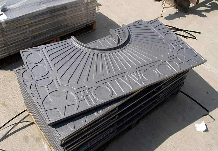 A stack of Ironsmith custom metal tree grate halves. There are raised stars in the corners and spell out Hollywood on each side.